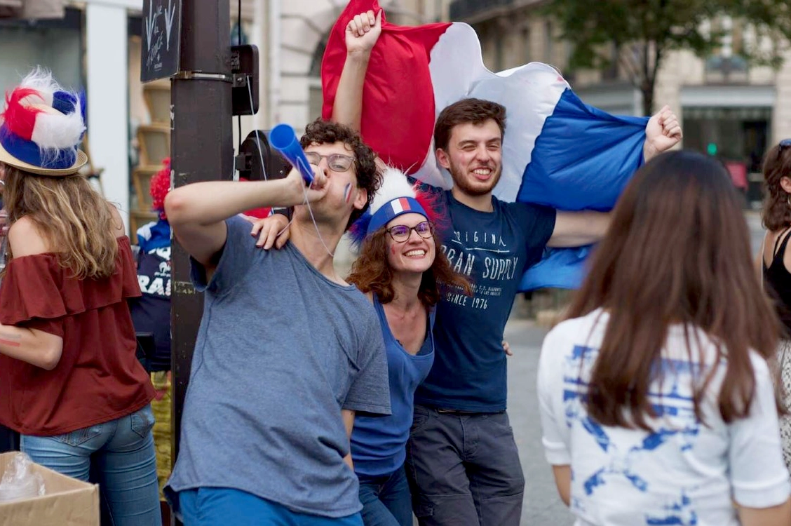 Group of young people celebrating in the street with French flags, face paint, and festive gear after France won a World Cup match.