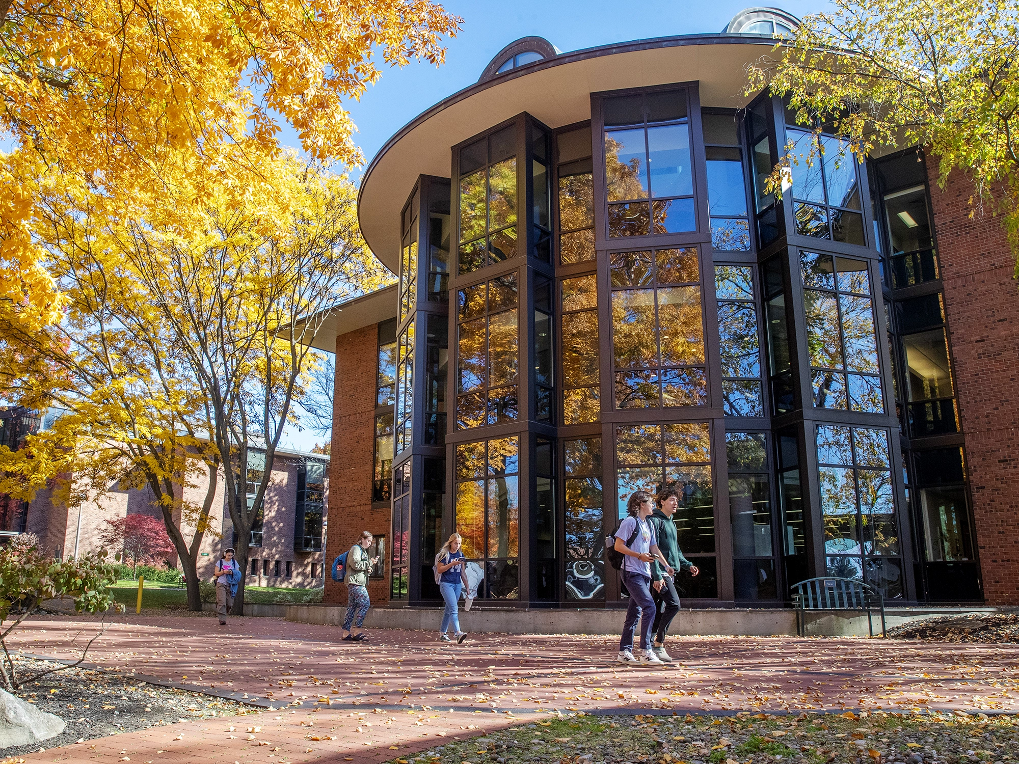 Skidmore College students walking past a glass-walled academic building surrounded by vibrant fall foliage on campus.