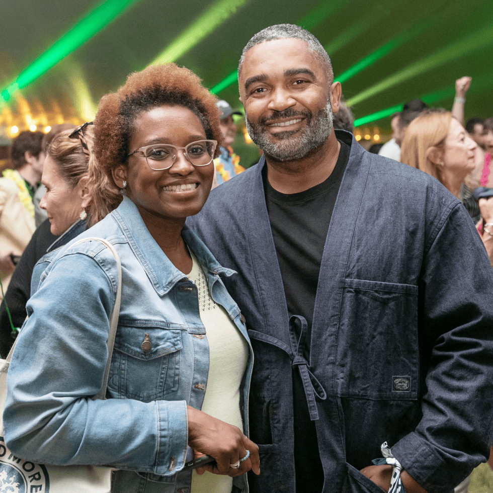 Two alumni celebrating under the tent at reunion with Skidmore green and yellow lights in the background.