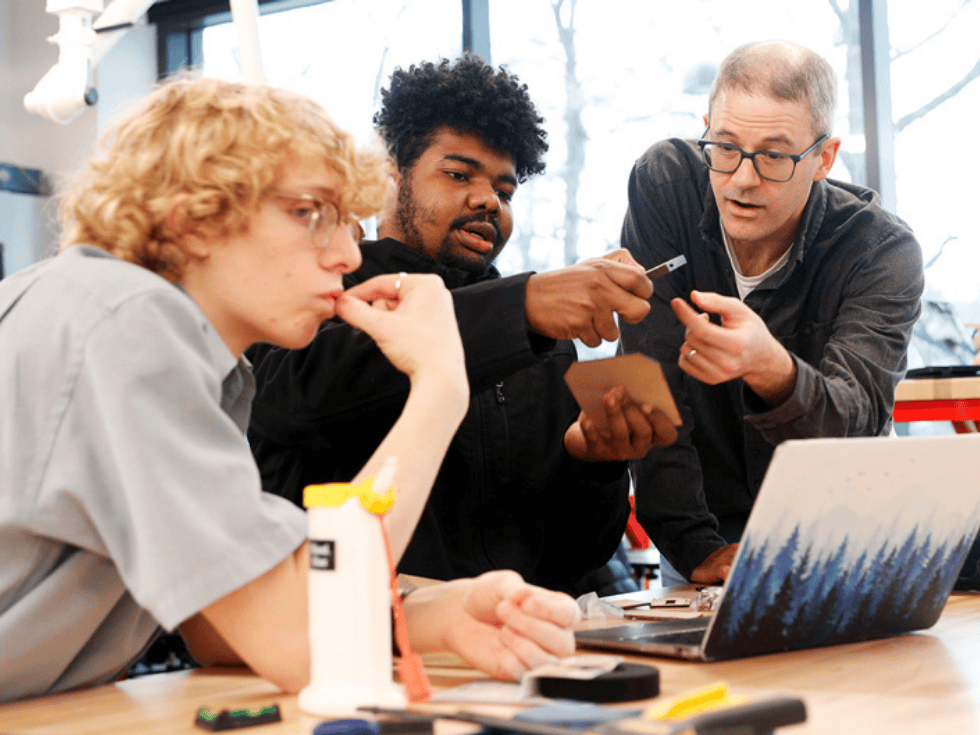 Two students working with a professor in the Idea Lab with a laptop computer.