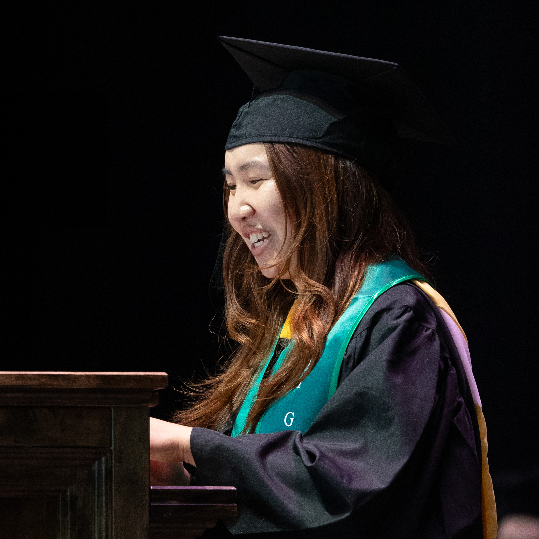 Madison Situ ’26 in cap and gown smiles while receiving recognition at the commencement podium.