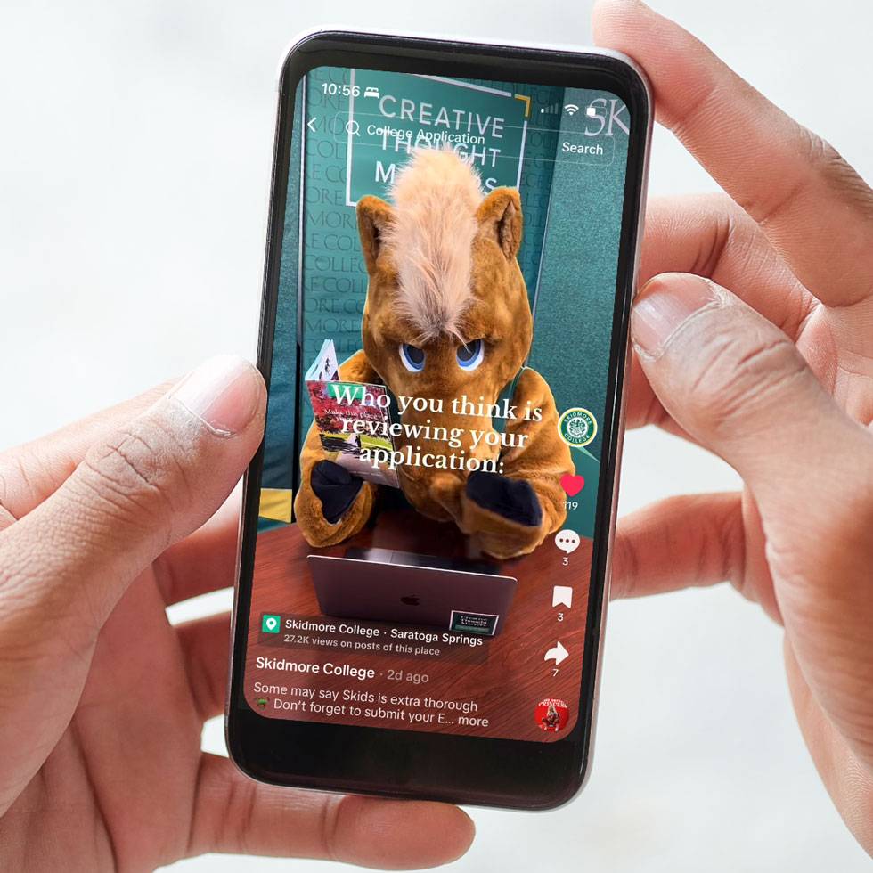 Hands hold a phone with a social media post highlighting Skidmore's mascot, Skids 