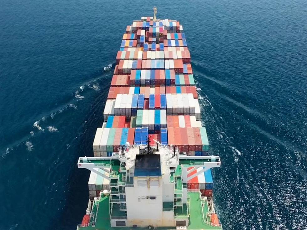 A freighter ship moves through dark blue water with different color shipping containers on board.