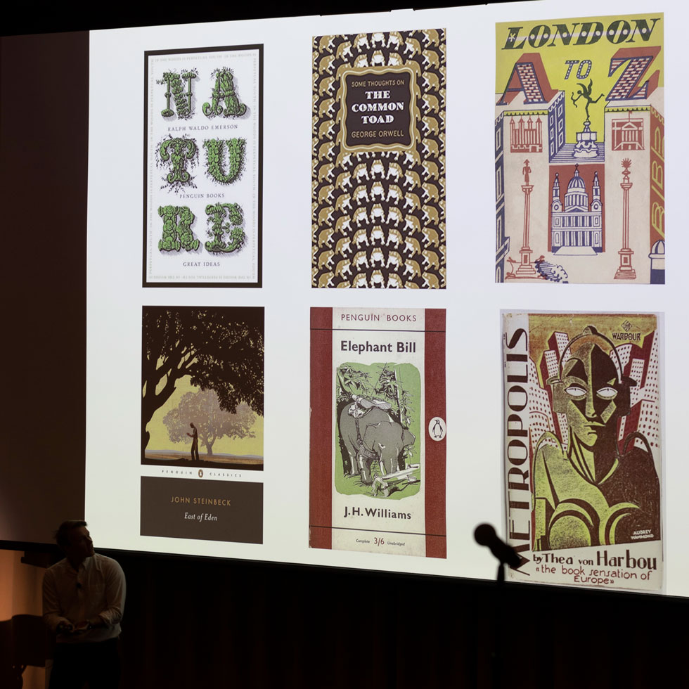 A speaker presents various illustrations on a screen in a lecture style room