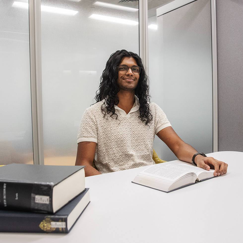 Peer student sits at a white desk in the a study room with books