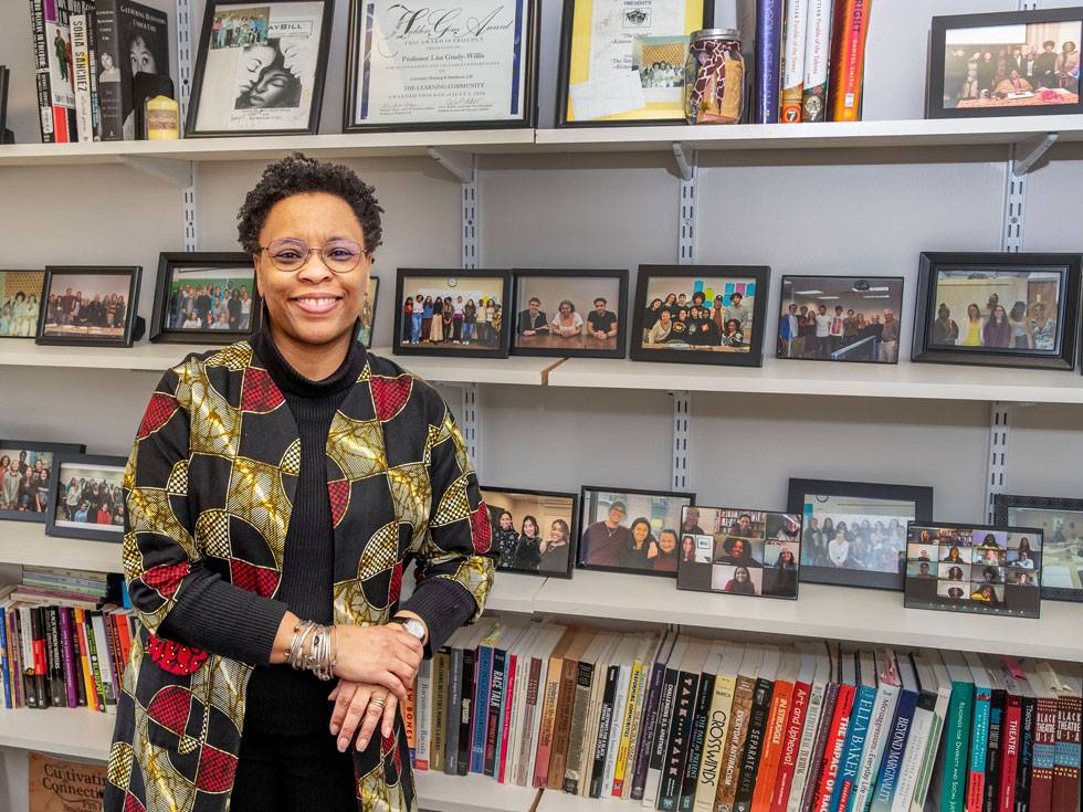 Lisa Grady-Willis stands in her office with her arm resting on shelves that include many photos and books. 