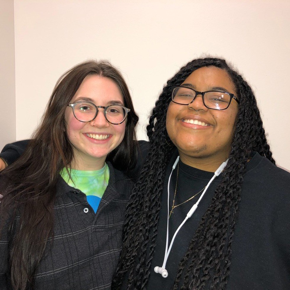 Two students stand together smiling.