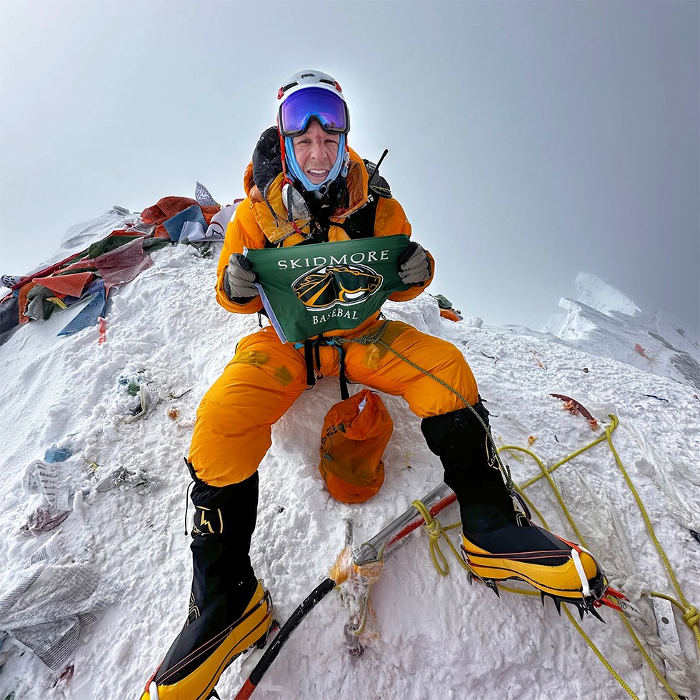 Matt Ferrari '05 holding a Skidmore Baseball flag at the summit of Mt. Everest.