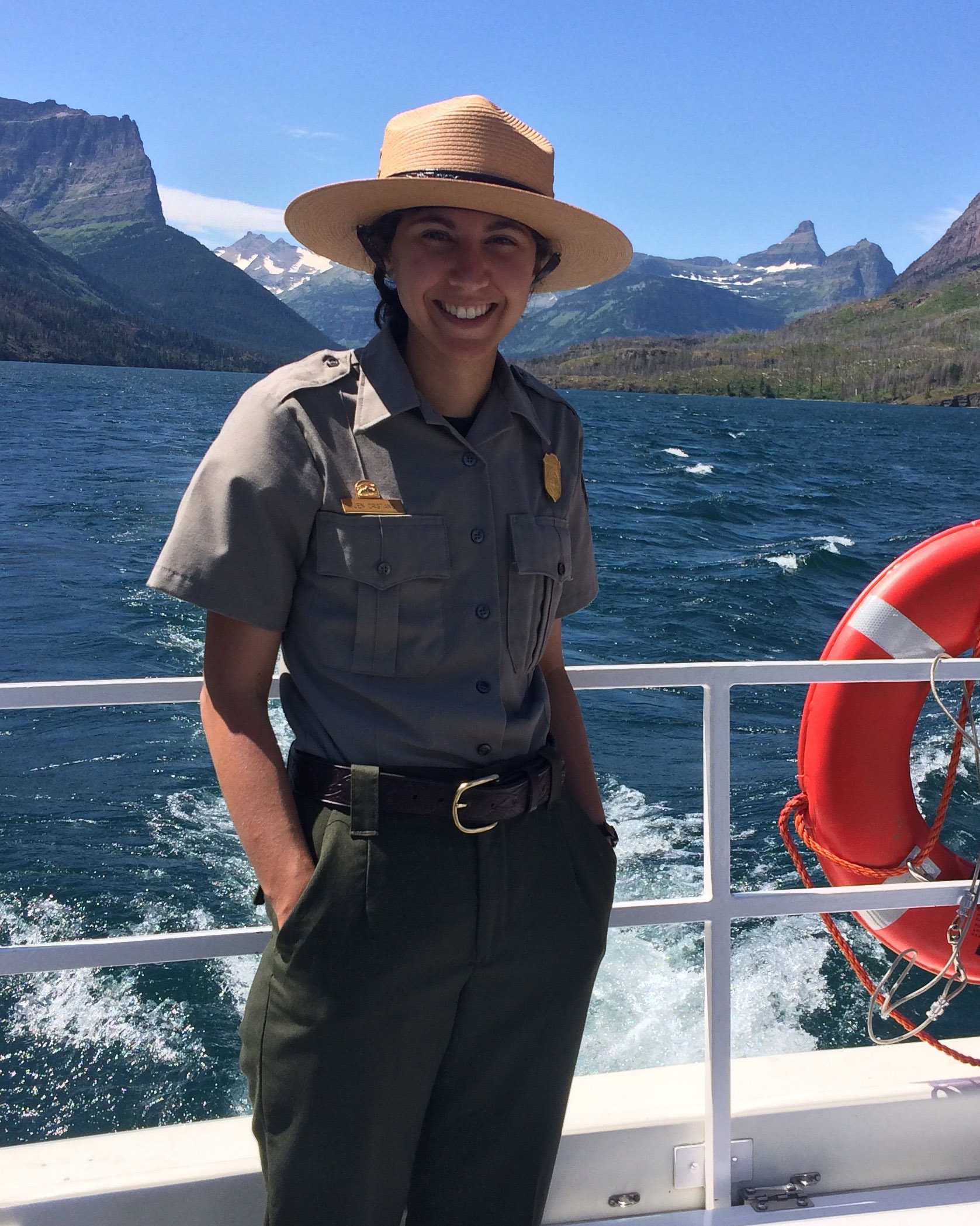 Jennifer Cristiano ’18 stands on the deck of a boat in her uniform. A range of mountains can be seen from across the water.
