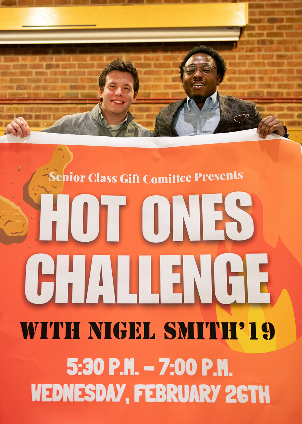 Nigel Smith ’19 and Austin Somers ’25 stand side by side, smiling and holding up a poster for the "Hot Ones" event.