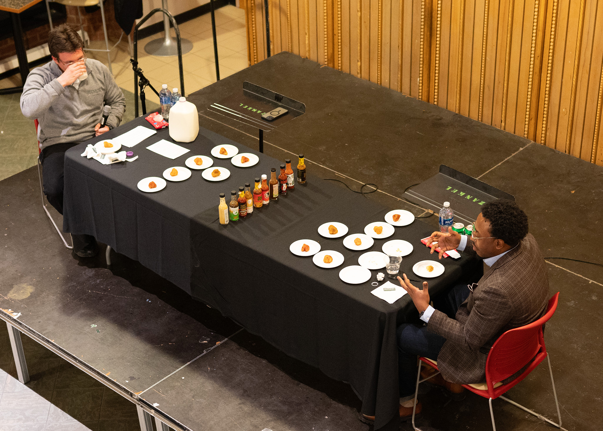 Nigel Smith ’19 and Austin Somers ’25 face off at a table on the stage at Case Center during the "Hot Ones" challenge.