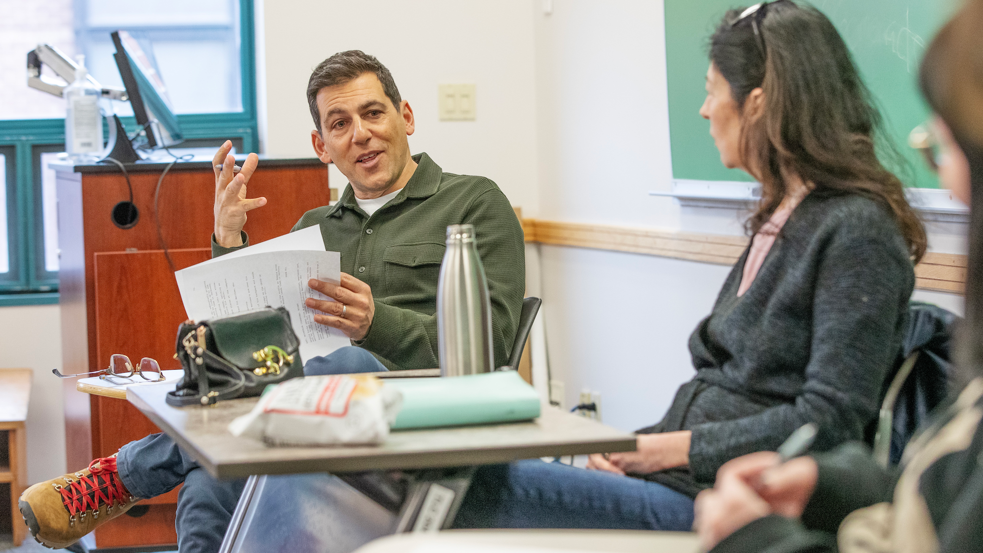 Zicherman reads from a student's screenplay during Nicole Coady’s MF 351 Advanced Screenwriting course, gesturing. Coady and a student can be seen siting to the right of him.