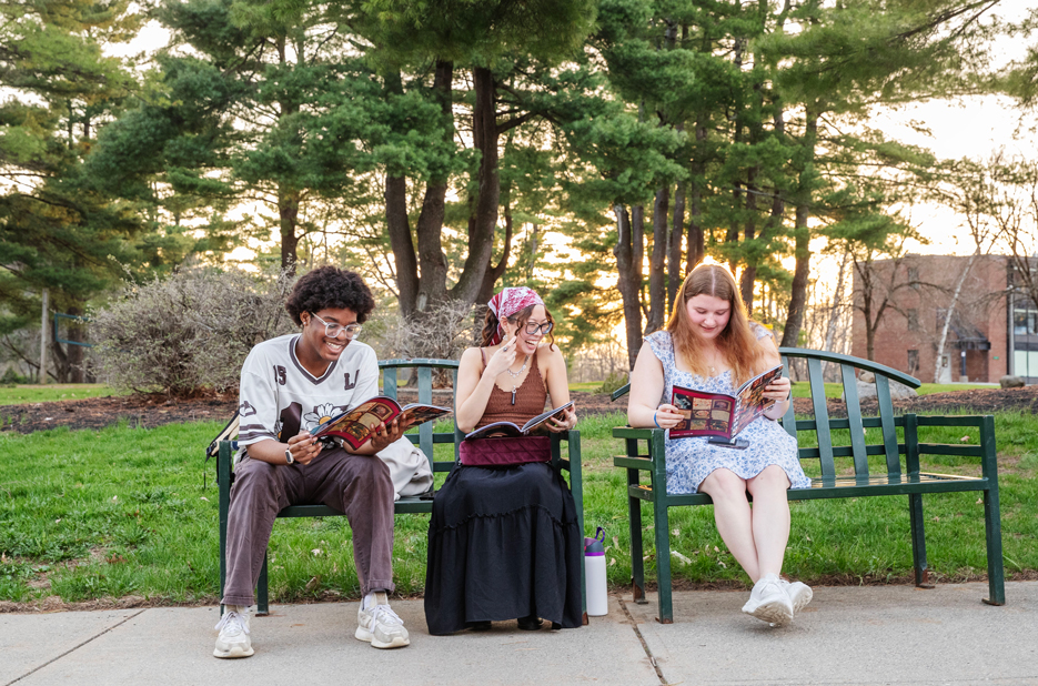 Three students sit on a bench outside the Tang Teaching Museum, looking through the latest issue of Lunchbox Magazine
