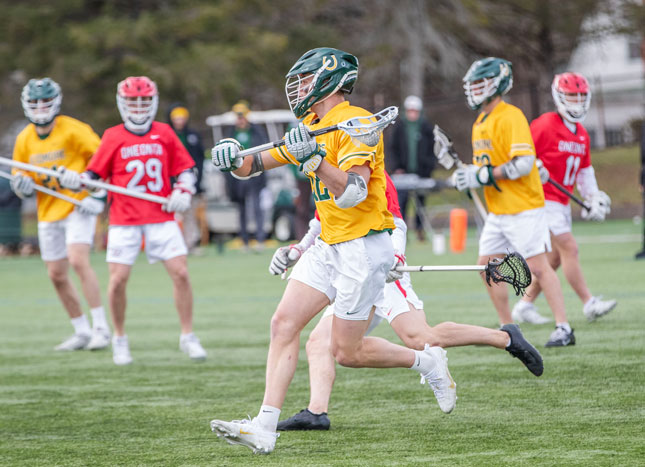 A Skidmore men’s lacrosse player in a yellow jersey carries the ball upfield during a game while players from Oneonta defend around him