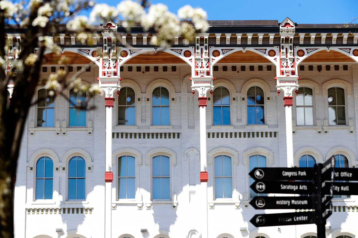 Historic Saratoga Springs building with decorative trim, arched windows, and wayfinding signs for local attractions.
