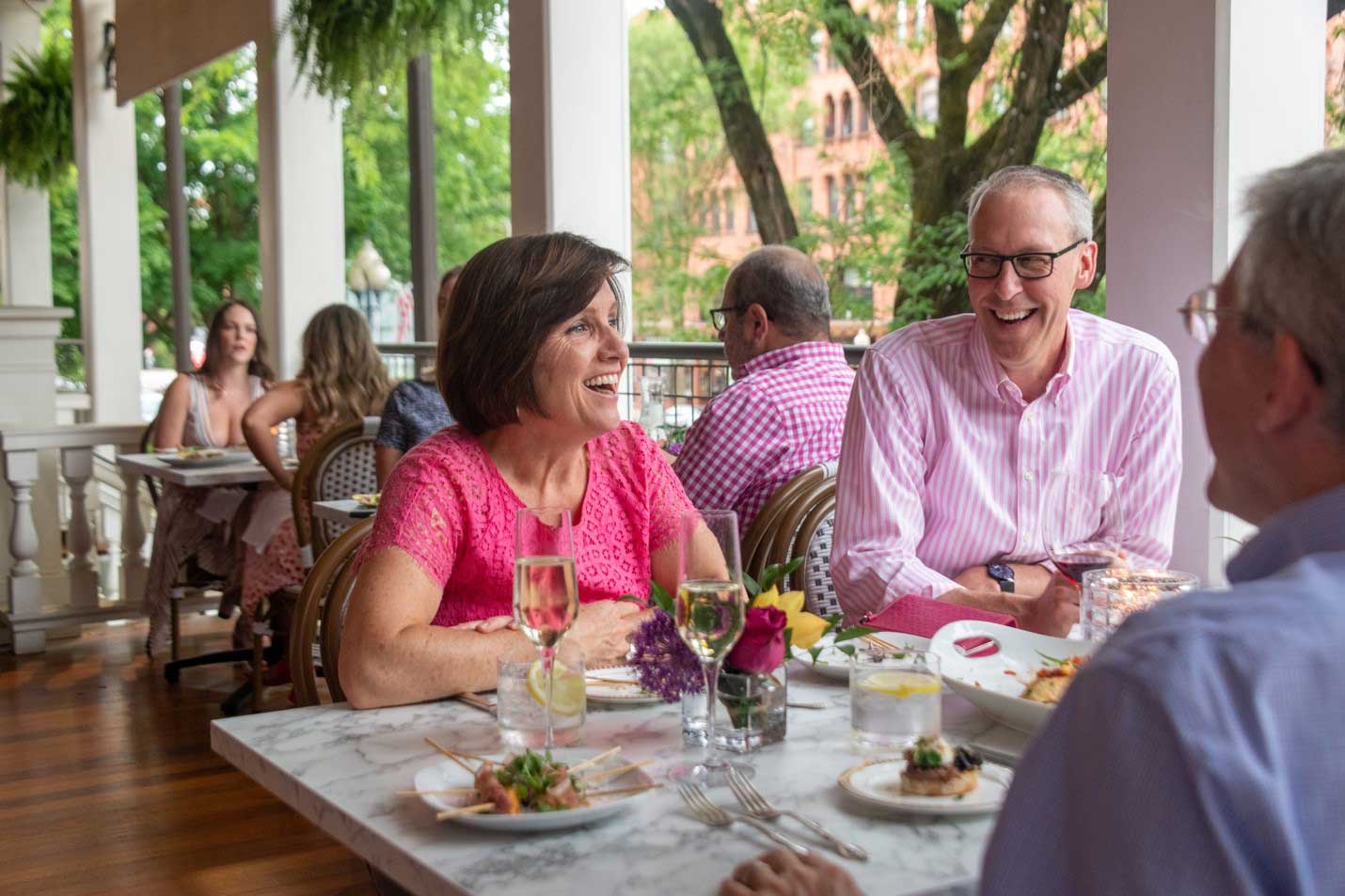 Adults laugh together while dining outdoors on a covered restaurant patio in downtown Saratoga Springs.