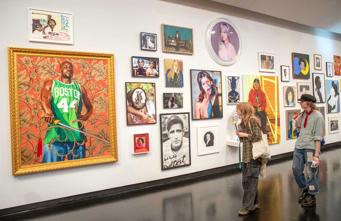 Two visitors view a gallery wall of contemporary portraits and artwork at Skidmore’s Tang Teaching Museum.
