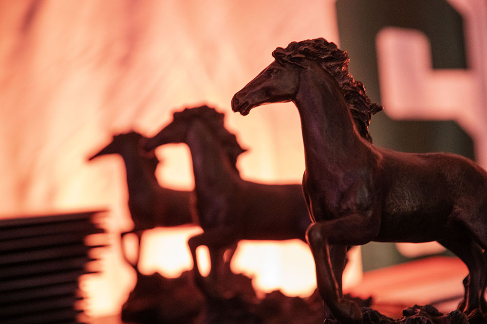 Horse statue trophies and a stack of certificates in booklets lined up on a table.