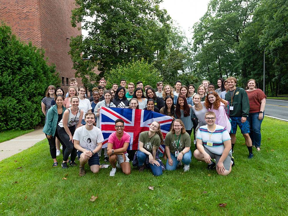 A large group of student stand on campus with a British flag in the center