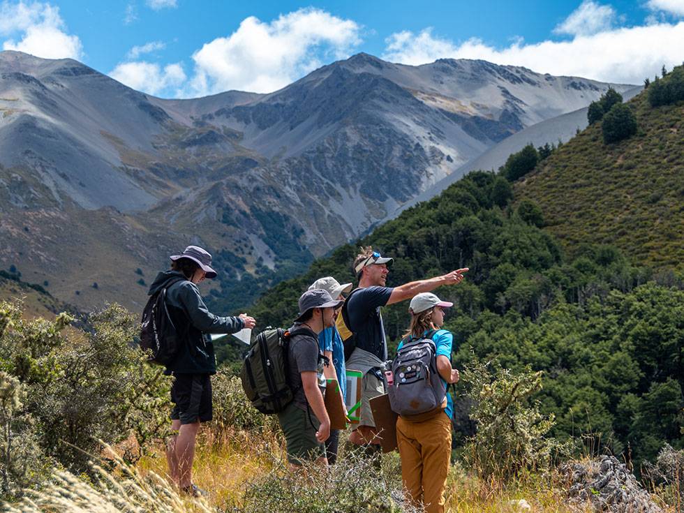 Students stand in mountains in New Zealand with a faculty member pointing to something in the distance. 