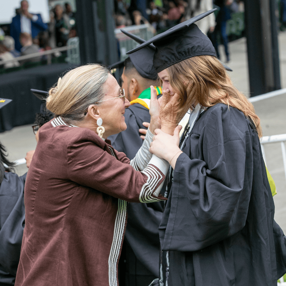 A parent embraces a graduates face warmly at commencement.