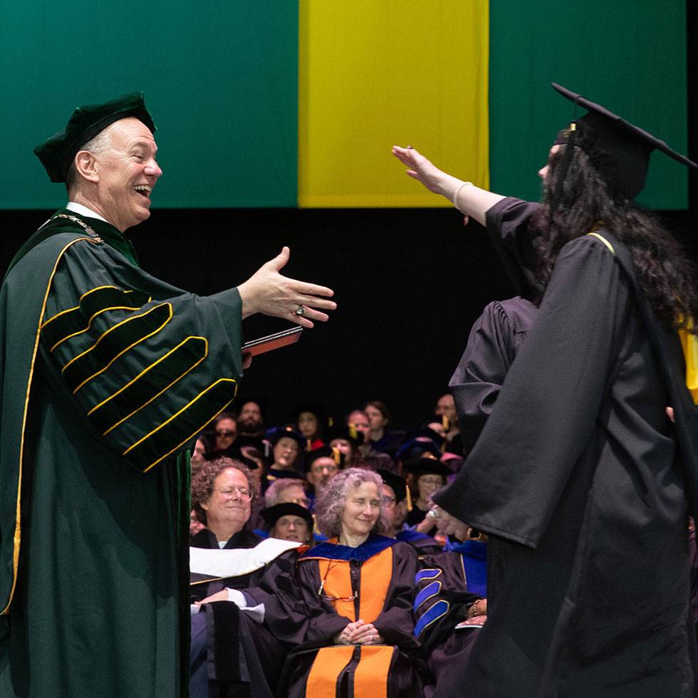 President Conner stands on stage at Commencement as a student graduates and they both get ready for a high five.