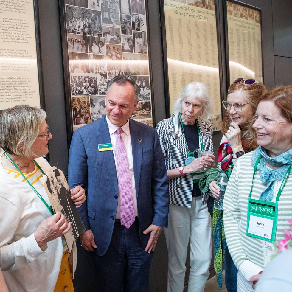 President Conner stands in a group of nursing alumni, listening intently as they speak with him.