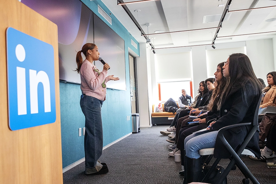 A LinkedIn employee speaks to a group of Skidmore College students during a presentation at LinkedIn headquarters in New York City, with a LinkedIn podium and large screen in the background.