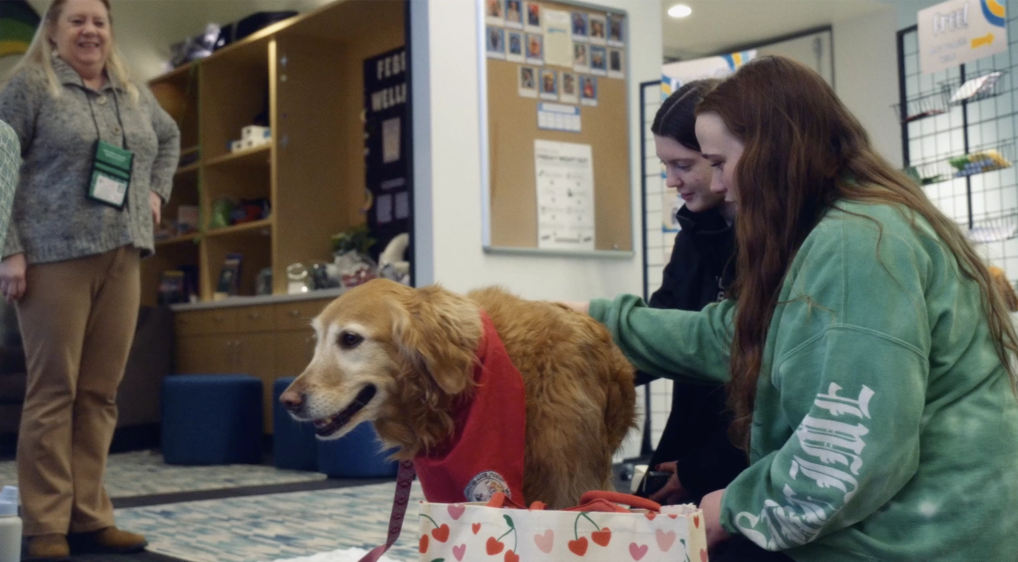 Two Skidmore College students pet a golden retriever therapy dog wearing a red bandana during a wellness event.