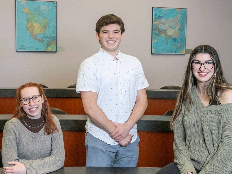 Three students pose while smiling in a lecture hall