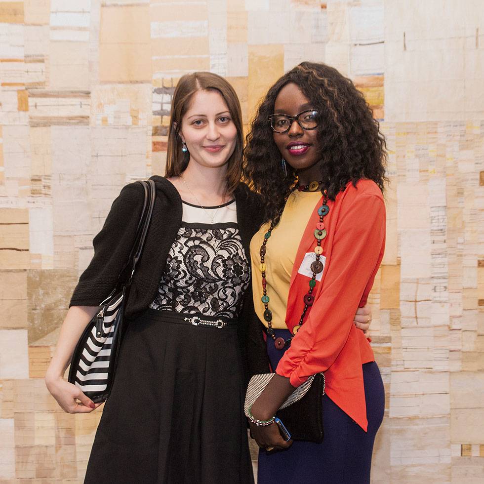 Two students pose with their arms around each others backs and a tan geometric backdrop