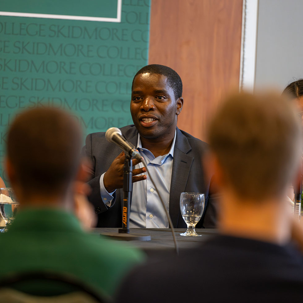 Students sits down at head table while speaking into a microphone with Skidmore green backdrop