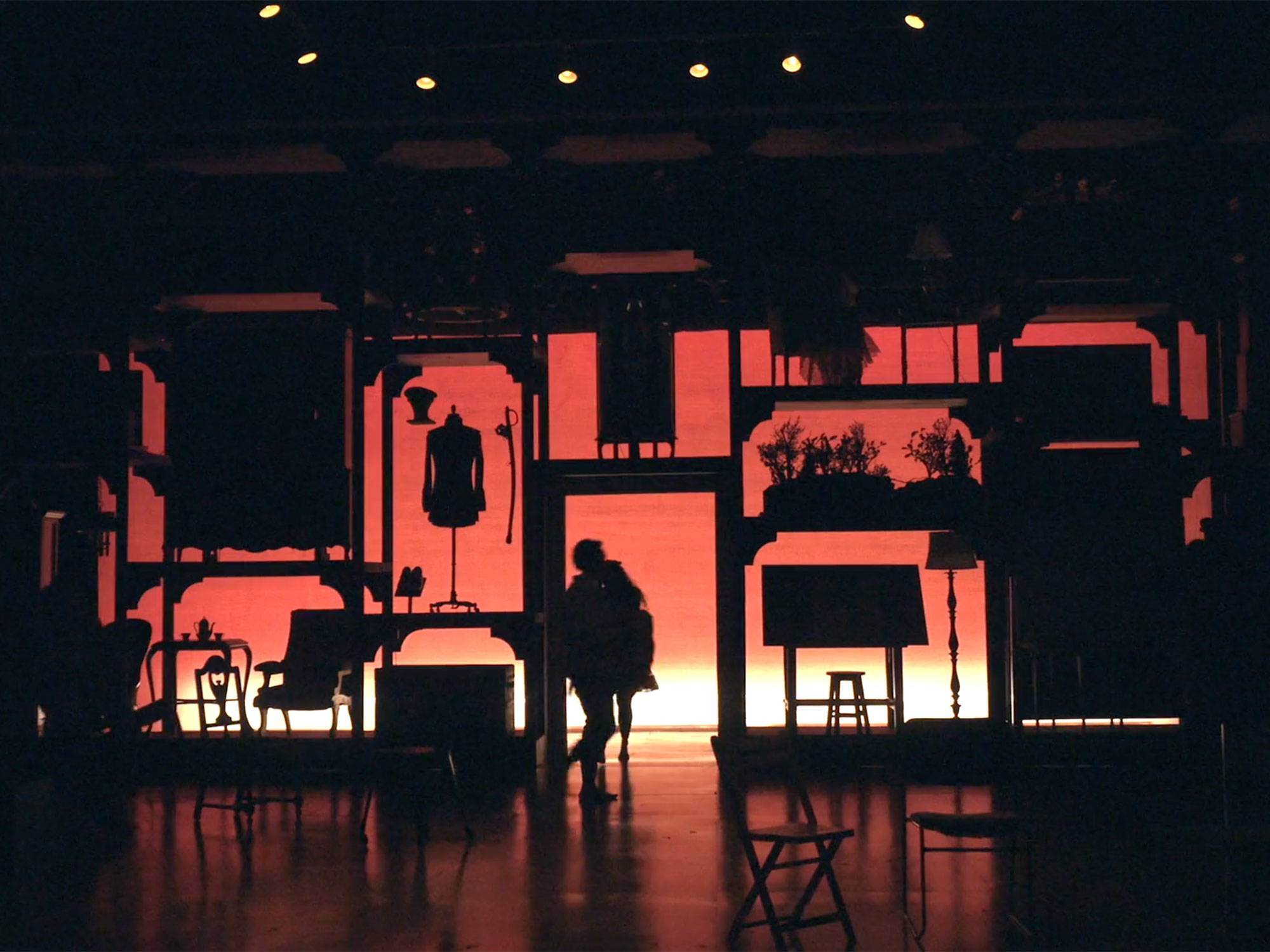 A dark stage backlit with orange hues show shadows of the stage set