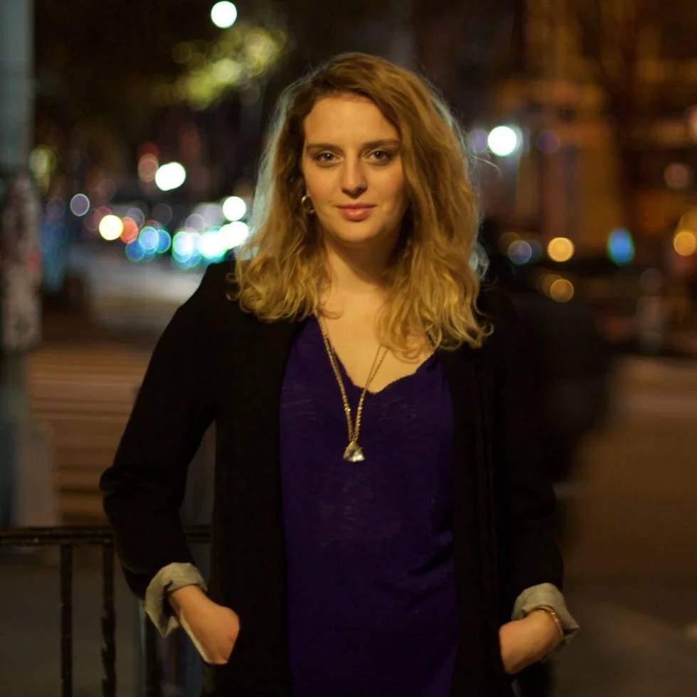 Erin Daley '09 stands outside with hands in her pockets and a dark city scape in the background.