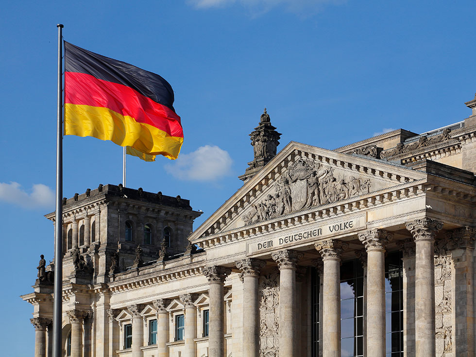 Reichstag building in Berlin with classical columns and a modern glass dome and German flag waving in a blue sky