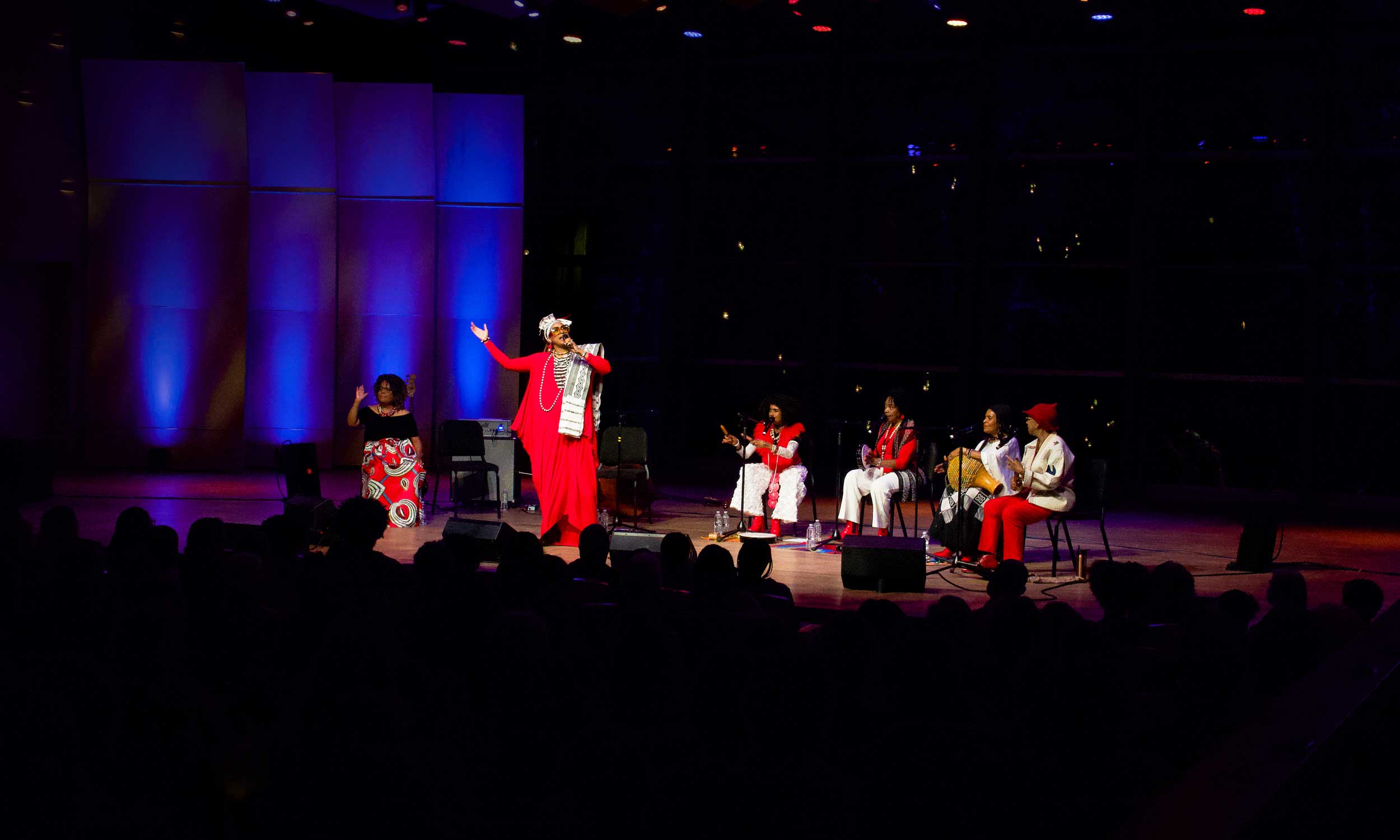 Vocalists perform onstage in Zankel Music Center under blue and purple lighting while an audience watches from the darkened concert hall.